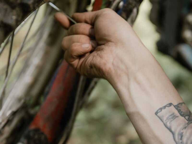 A tattooed hand works on a motorcycle tire in a detailed outdoor close-up.
