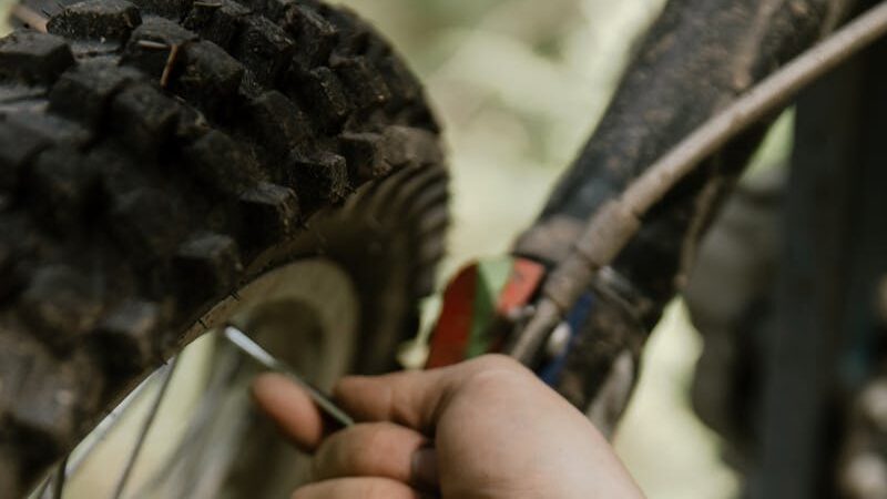 A tattooed hand works on a motorcycle tire in a detailed outdoor close-up.